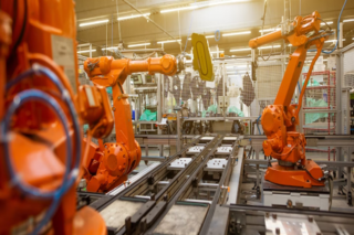 Big orange machinery arms in a production line of a well lit factory.