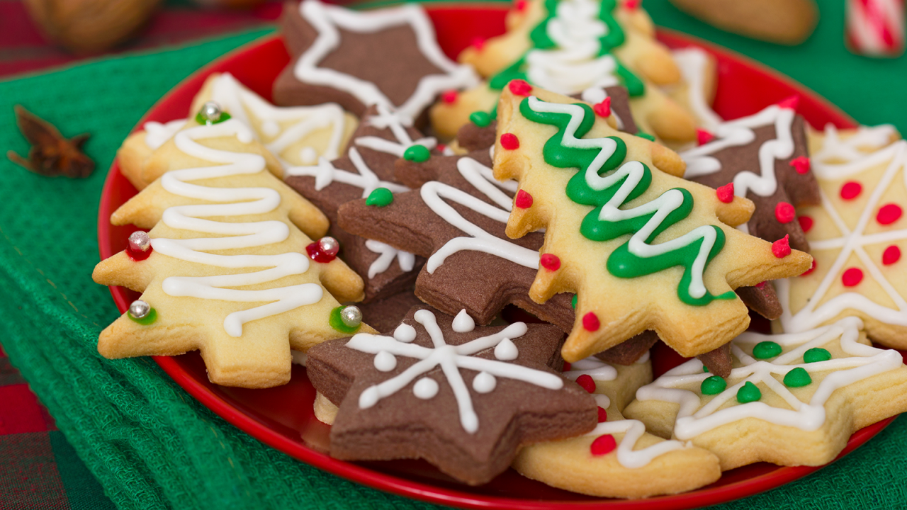 Prato vermelho cheio de biscoitos de Natal sobre uma toalha de mesa verde.
